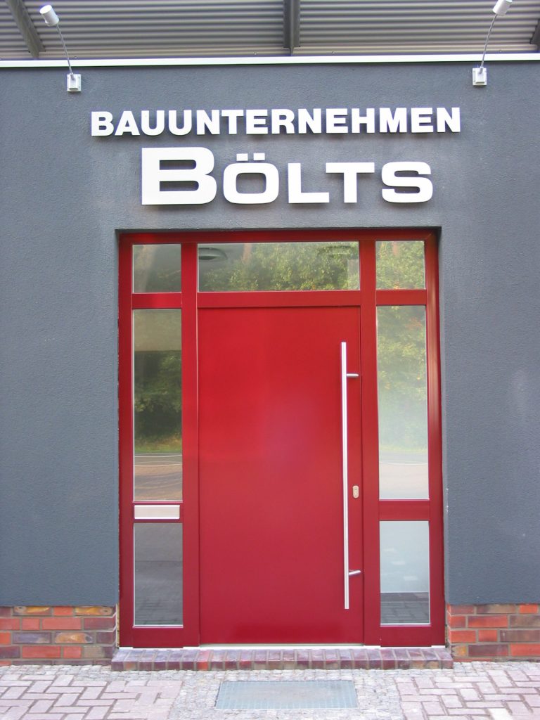 Eingangsbereich des Bauunternehmens Bölts mit roter Tür und grauer Fassade.